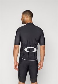 Schwarzes Radtrikot mit kurzen Ärmeln, elegantes Design und elastischem Rücken. Verfügt über ein auffälliges weißes Logo und eine enge Passform, ergänzt durch schwarze Radhosen.