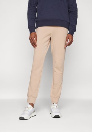 Sudadera beige con un ajuste ajustado y cinturilla elástica. Combinada con zapatillas blancas que cuentan con acentos de malla y texturizados.