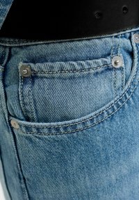 Gros plan d'une poche de jean en denim bleu avec rivets métalliques et partie d'une ceinture en cuir noir avec des trous.