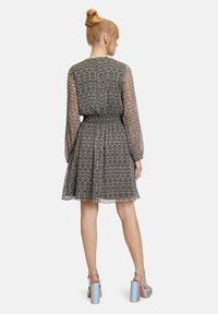 Schwarzes und weißes gemustertes Kleid mit langen, transparenten Ärmeln, tailliertem Schnitt und ausgestelltem Rock. Silbern blockabsatzige Sandalen runden das Outfit ab.