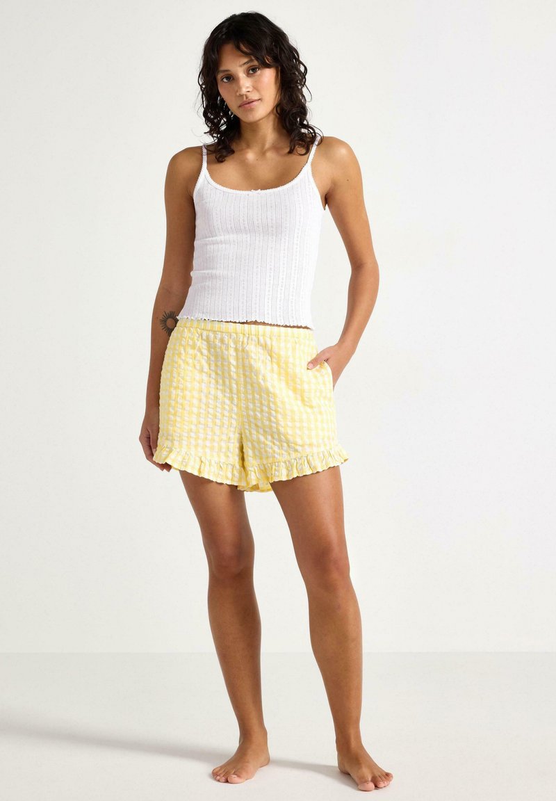 Hvid ribbet tanktop og gule ternede shorts med bølget kant. Sættet har en afslappet pasform og let materiale.