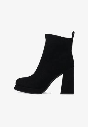 Zwarte suède enkelboots met een hoge blokhak en een platformzool. Voorzien van een lus aan de achterkant en een strakke, minimalistische stijl.