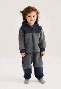 Grijs en marineblauw hoodie- en broekset in kleurvlakken, gemaakt van zachte stof. Voorzien van een ritssluiting aan de voorkant, elastische manchetten en een capuchon. Gestructureerde afwerking.