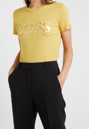 Geel T-shirt met korte mouwen en metallic "BOSS" logo, gecombineerd met zwarte hoge taille broeken met riemlussen en zijzakken.