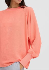 Felpa coral con scollo a girocollo a costine, maniche lunghe a raglán e vestibilità rilassata. Tessuto morbido e texture.