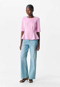 Rosa peplumtop med korta ärmar, matchat med ljusblå vida jeans och svarta klackar med remmar. Slät textur, enkelt design.