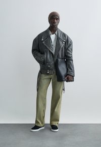 Black leather biker jacket, plaid shirt, white t-shirt, green wide-leg trousers, black handbag, and black sneakers with white soles.