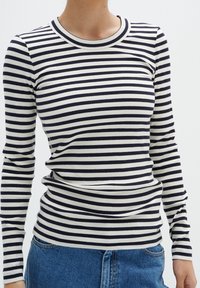 Haut à manches longues rayé en tissu côtelé bleu marine et blanc cassé. Il présente un col rond et un corps ajusté, avec de légers fronces à la taille.