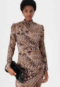 Kjole med leopardtrykk, lange ermer, høy hals og drapert design. Kombinert med en svart blank håndveske.