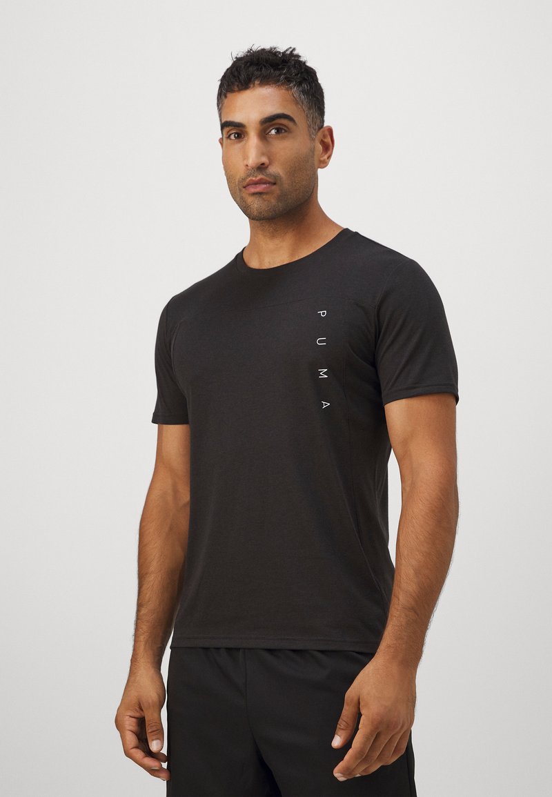 Camiseta preta de manga curta feita de algodão, com um corte justo e um logótipo branco vertical do lado esquerdo. Textura suave.
