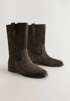 Stivali alti in suede marrone con punta rotonda, suola piatta in gomma e linguette posteriori; texture liscia e dettagli di design senza cuciture.