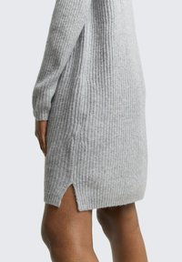 Robe pull grise à côtes avec des manches longues, fentes sur les côtés à l'ourlet, texture douce et silhouette ajustée.