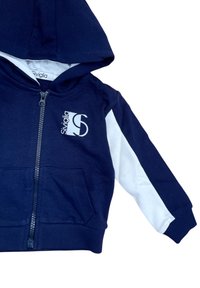 Felpa con cappuccio navy con pannelli laterali bianchi, chiusura zip frontale e tasca a marsupio. Presenta una grafica con logo e un tessuto morbido e texturizzato.