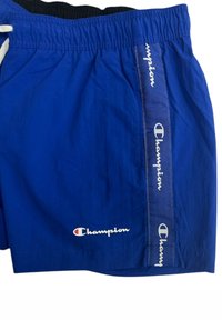 Costumi da bagno blu con una cintura elastica, cordino bianco e decorati con il logo "Champion" in bianco lungo la cucitura laterale.