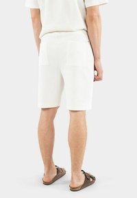 Vita ribbade bomullsshorts med två bakfickor, rak skärning och en nederkant som slutar ovanför knäet, i kombination med bruna slides.