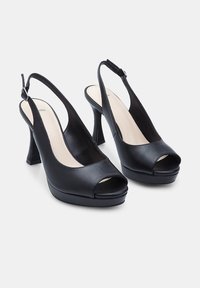 Crne slingback visoke potpetice s otvorenim prstima, glatka kožna površina, srednja visina potpetice i platforma. Podesiv remen s detaljima kopčanja.