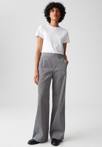 Grijze corduroy wijde broek met een hoge taille, voorzakken en een gestructureerde afwerking, gecombineerd met een plain wit T-shirt. Zwarte schoenen zichtbaar.