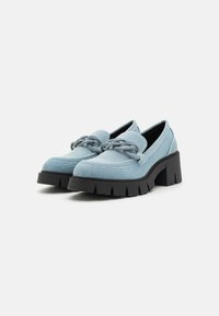 Light blue denim loafers with a chunky black sole, featuring decorative chain accents on the front and a smooth texture.