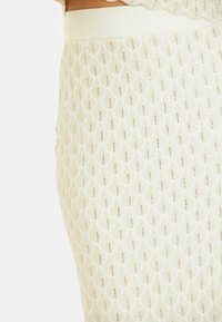 Strickrock in Creme mit einem zarten Blattmuster und subtilen metallischen Akzenten, weicher Textur und einem glatten, elastischen Bund.