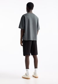 T-shirt gris en coton, coupe ample, avec un short noir. Baskets blanches, semelles crème, et chaussettes blanches à liseré noir. Design simple, sans motifs.