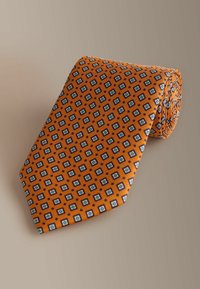 Narancssárga selyem nyakkendő, kék-fehér ismétlődő gyémántmintával, texturált felülettel. Semleges háttéren feltekerve bemutatva.