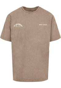 Rudas per didelį T-marškį, pagamintą iš medvilnės tipo medžiagos, priekyje yra baltos raidės "NEKREIPK DĖMESIO" ir "BEARLY A.W.A.K.E".