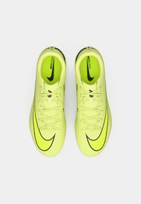 Fényes sárga focicipők texturált felülettel, fekete kiegészítőkkel és hangsúlyos Nike logóval. Hagyományos fűzéssel és párnázott talpbetéttel rendelkeznek.