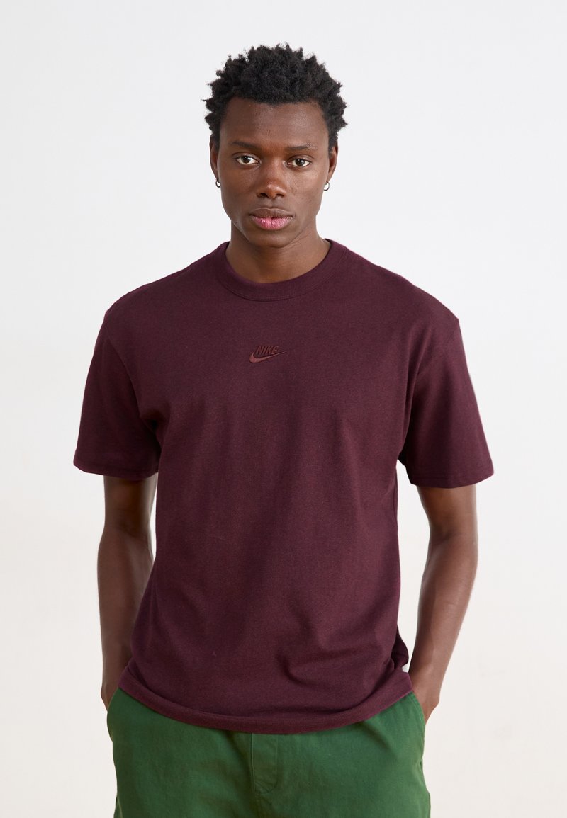 Bordeaux-koton T-paita lyhyillä hihoilla, pyöreä kaula-aukko ja pieni, kohokuvioitu Nike-logo rintakehässä, yhdistettynä vihreisiin shortseihin.