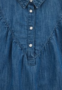 Tums džinsu krekls tumši zils, ar apkakles izgriezumu, pērļu pogām un plecu un sānu daļās izgrieztu audumu detaļām.