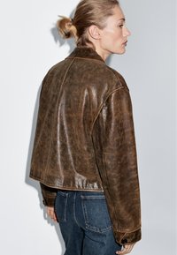 Bruine leren cropped jas met een slank ontwerp, een gladde textuur en knoopaccenten, gecombineerd met donkerblauwe denim broeken.