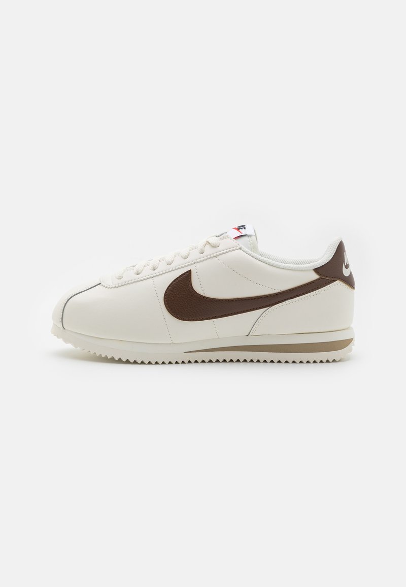 Baskets en cuir blanc avec un swoosh marron, dotées d'un bout arrondi, d'une fermeture à lacets et d'une semelle en caoutchouc texturée, avec un subtil accent de logo.