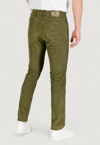 Pantaloni in corduroy verde olive con una vestibilità affusolata, dotati di tasche posteriori, una texture sottile e un'etichetta del marchio sulla vita. Sneakers bianche visibili.