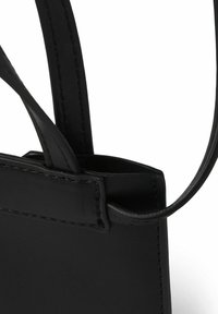 Czarna skórzana torba o gładkiej fakturze, cienkich paskach i prostokątnym kształcie. Widoczne detale przeszycia podkreślają design.