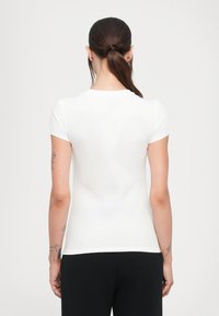 Witte getailleerde t-shirt met korte mouwen, gladde textuur en een klassieke ronde hals, gezien vanaf de achterkant. Geen zichtbare patronen of accenten.