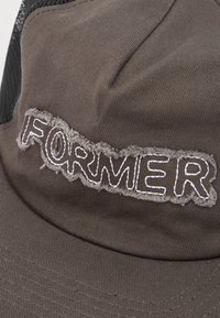 Καφέ υφασμάτινο καπέλο με μια πατς με σκληρές άκρες που εμφανίζει τη λέξη "FORWER" κεντημένη με λευκή κλωστή στο μπροστινό πάνελ.