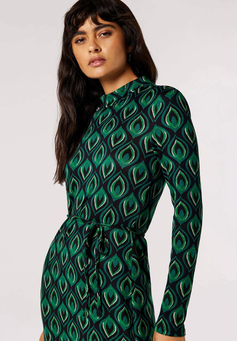 Abito a maniche lunghe verde e nero con motivo a foglie, caratterizzato da un colletto alto e una cintura legata in vita per una silhouette aderente.