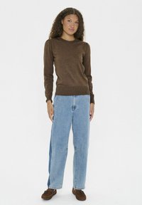 Brun, stickad tröja med ribbade ärmslut och nederkant, i kombination med ljusblå, vida jeans med fickor och synliga sömmar. Bruna skor.