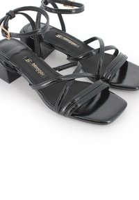 Sandalias negras con tiras, con un acabado brillante, punta cuadrada y tacón ancho. Presentan múltiples tiras cruzadas y una plantilla con la marca.