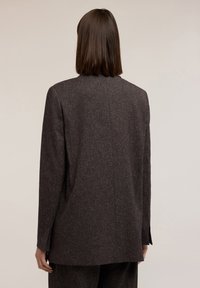 Dunkelbrauner maßgeschneiderter Blazer aus strukturiertem Stoff, mit einem schlichten, geraden Schnitt, Reverskragen und einem einzelnen Schlitz auf der Rückseite.