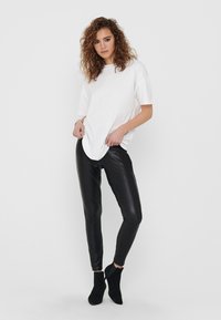 White oversized t-shirt paired with black faux leather leggings and black ankle boots. Smooth textures and fitted silhouette.