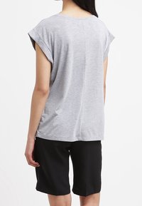 Harmaa lyhythihainen paita, jossa on käännetyt hihansuut, rento malli ja suora takasauma, yhdistettynä mustiin šortseihin, joissa on sileä kangas ja polvipituus.