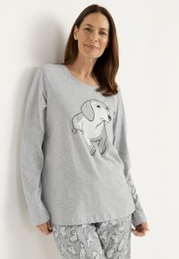 Grå långärmad tröja med en svart konturillustration av en hund på framsidan, ihop med grå byxor prydda med hundmönster.