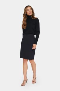 Pulover negru cu guler înalt, asortat cu o fustă creion neagră, ajustată. Modelul poartă sandale cu toc înalt și curea, evidențiind o siluetă elegantă.