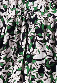 Blumenkleid mit einem dunkelblauen Hintergrund, weißen und grünen Blumen, tailliert mit einem Bogen-Detail und weichem Stoffgefühl.