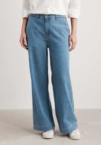 Jeans ampi in denim blu chiaro, caratterizzati da una vita alta, chiusura con bottone e una vestibilità rilassata. Dettaglio di cucitura sottile lungo l'orlo.