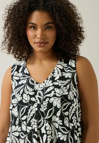 Ärmlös topp med V-ringning, med en svart bakgrund och vitt blommönster. Lättviktig tyg med en texturerad yta.