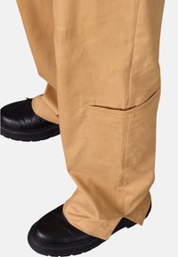 Khaki pants with a relaxed fit, made of lightweight material. Features a side pocket, worn with black boots and a slightly rolled hem.