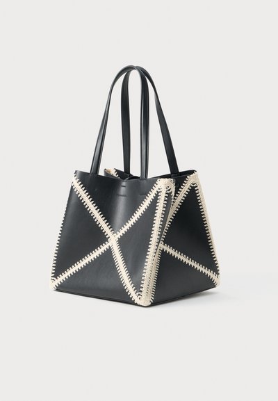 Black leather tote bag featuring cream stitching in a geometric pattern, with two sturdy handles and an open top design.