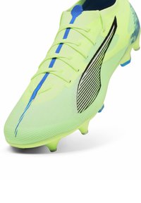 Scarpa da calcio gialla brillante con parte superiore in rete, lacci blu e design laterale nero. Presenta una suola testurizzata e punte stampate per una migliore aderenza.