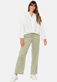 Blusa bianca a maniche lunghe con chiusura a bottoni abbinata a pantaloni palazzo in corduroy verde chiaro. Modella che indossa scarpe da ginnastica bianche.